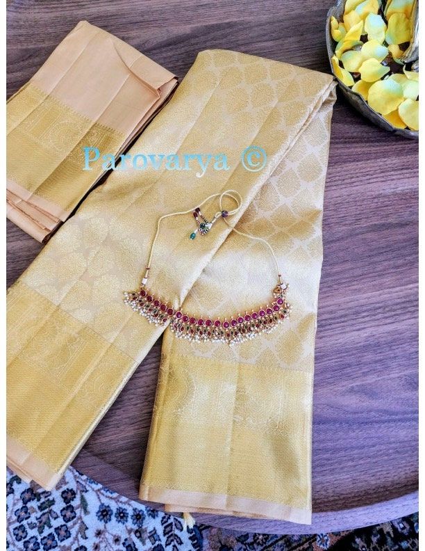 A marvelous gold-tone Kanjeevaram with a traditional gold zari and pallu. This is a pure silk handloom saree. The saree comes with a gold blouse but can be best contrasted with a red or bright blouse. The jewelry in the image is for display purposes only and does not come with the saree. Saree is complete with fall and pico. Minimum color variations are expected due to high-resolution camera quality. Gold Traditional Wear With Tilla Embroidery, Gold Katan Silk Blouse Piece With Self Design, Traditional Gold Blouse Piece For Wedding, Gold Anarkali Banarasi Silk Blouse Piece, Gold Saree With Self Design For Puja, Gold Raw Silk Pre-draped Saree With Self Design, Gold Pre-draped Raw Silk Saree With Self Design, Traditional Gold Handloom Blouse Piece, Gold Designer Wear Saree With Self Design