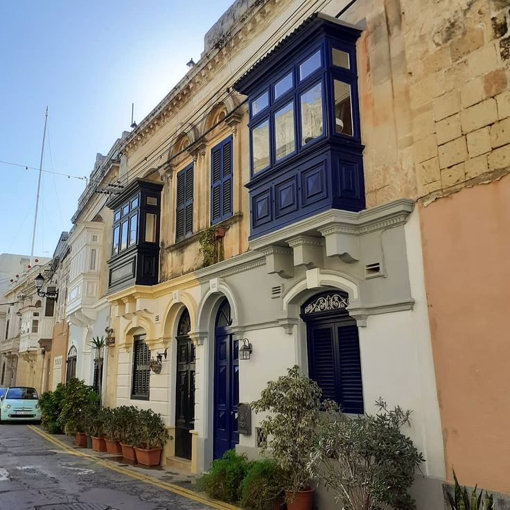 an old building with blue windows and shutters on the outside, along side potted plants