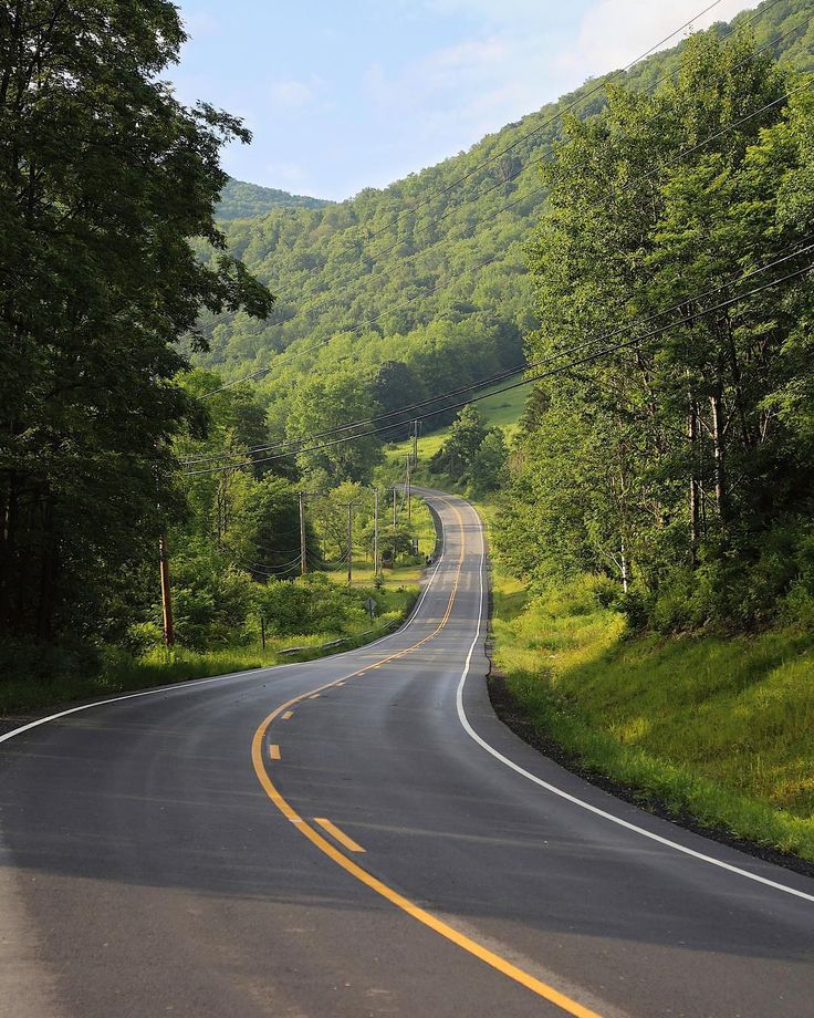 an empty road surrounded by trees and hills