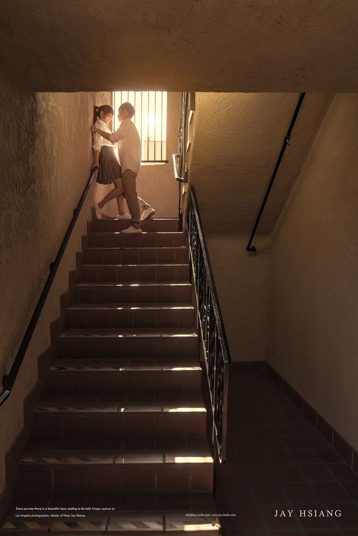 two people walking up some stairs with their arms around each other and the light coming through them