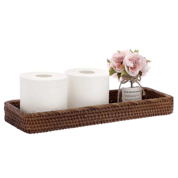 two rolls of toilet paper sitting on a wicker tray next to a vase with flowers