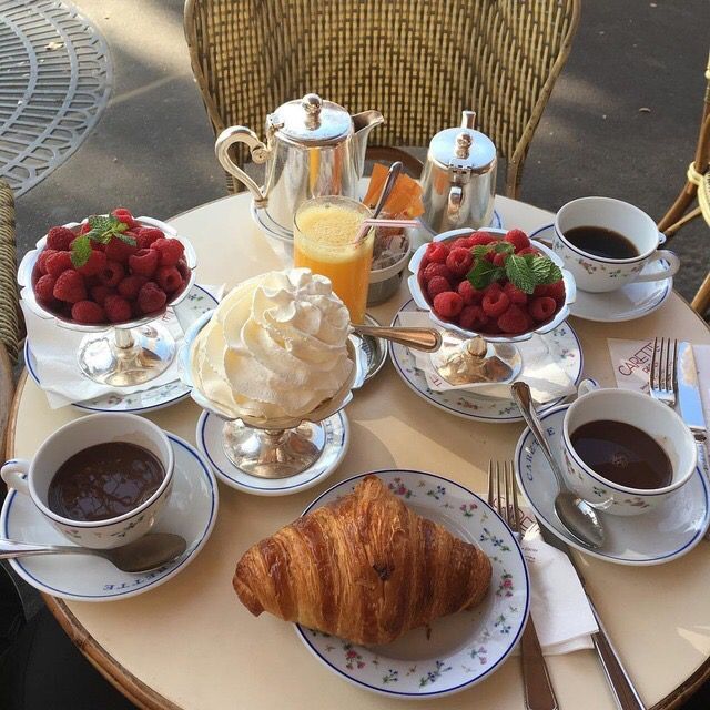 a table topped with plates of food next to cups of coffee and croissants