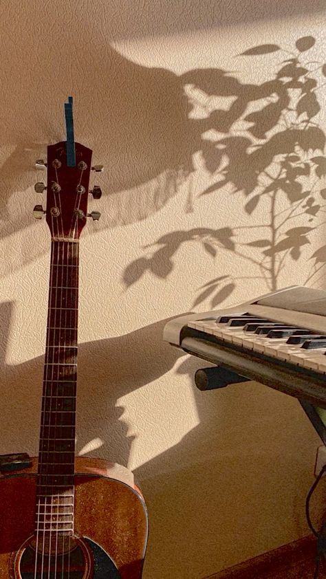 an acoustic guitar sitting in front of a piano keyboard and shadow on the wall behind it