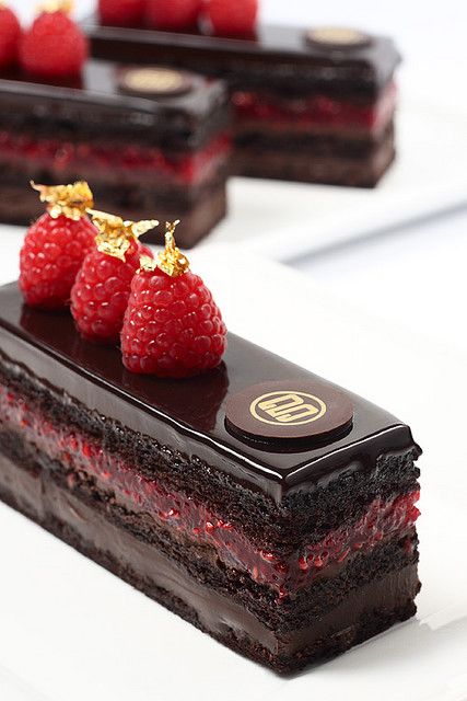 chocolate cake with raspberries on top sitting on a white plate next to other desserts