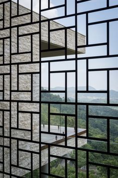 the view through an open window at a building with mountains in the background and trees