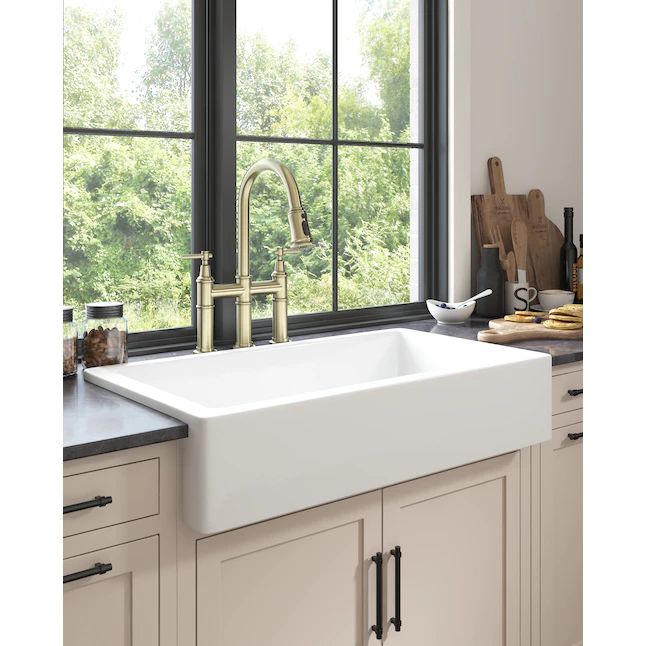 a white kitchen sink sitting under a window next to a wooden cutting board and utensils