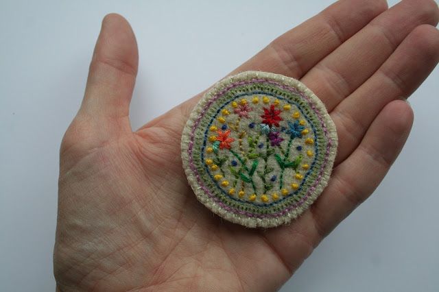 a hand holding a small embroidered brooch with flowers on it's center and sides