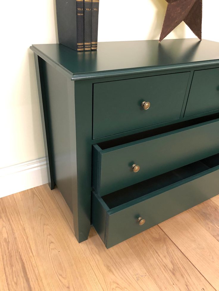 a green dresser with two drawers and books on top