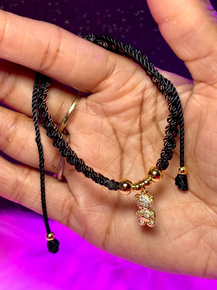 a hand holding a black string bracelet with gold beads and charms on it's wrist