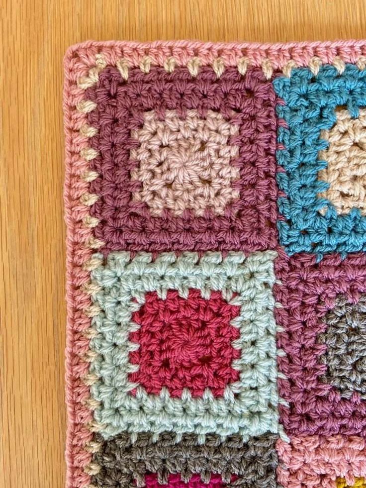 a crocheted square is shown on a wooden surface with the squares in different colors