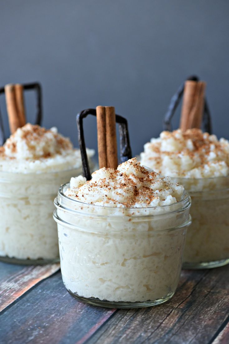 three small glass jars filled with food on top of a wooden table and cinnamon sticks sticking out of them