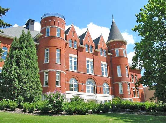 a large red brick building with many windows and turrets on it's sides, in front of some trees