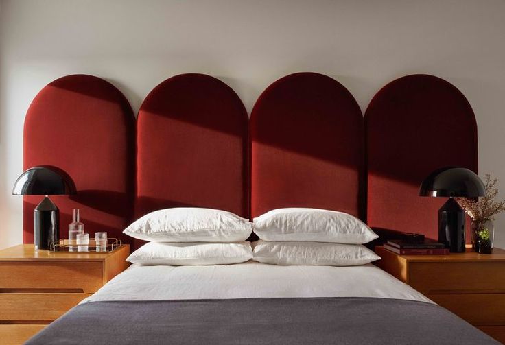 a bed with pillows and two lamps on either side of it in front of three red headboards