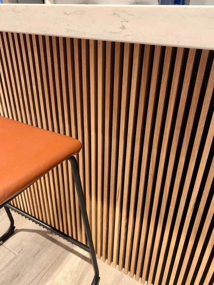 an orange chair sitting in front of a wooden slatted wall with metal legs