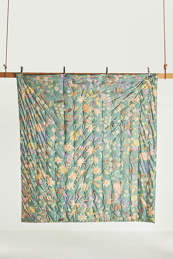 a green and yellow flowered blanket hanging from a clothes line with two wooden pegs