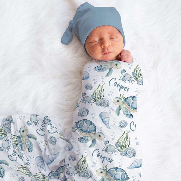 a baby is sleeping on a white blanket and wearing a blue hat with sea animals