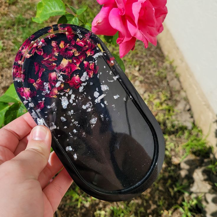 a hand holding a computer mouse in front of a pink flower and green grass with white speckles on it