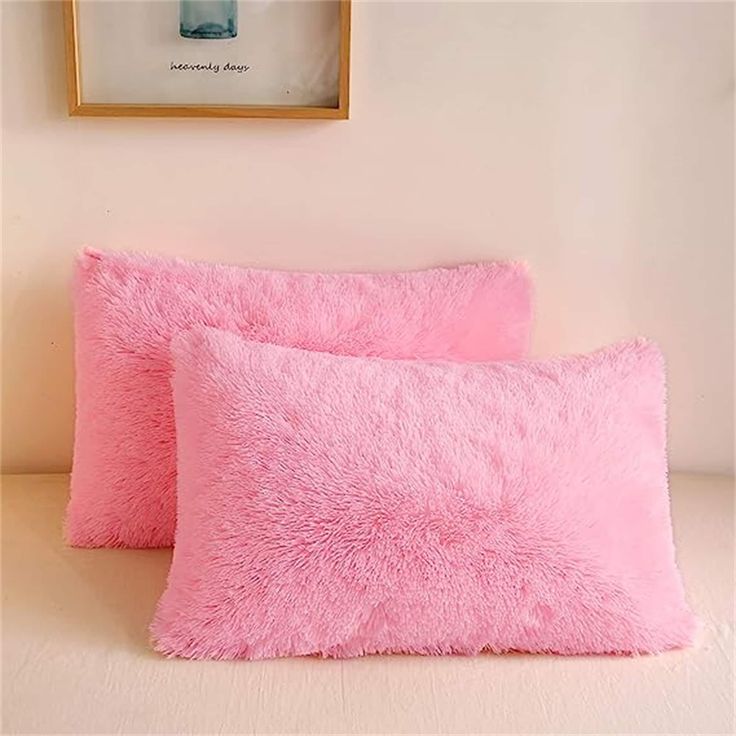 two pink pillows sitting on top of a white bed next to a framed photograph and a painting