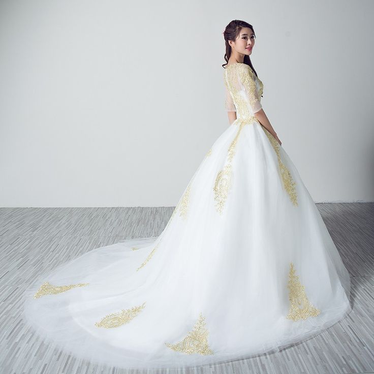 a woman in a white and gold wedding dress standing on the floor with her back to the camera