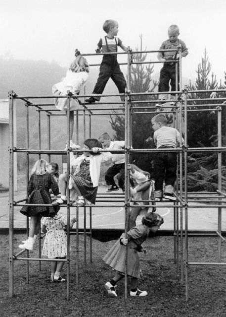 children playing on a play structure made out of metal pipes and tubes, in an old black and white photo