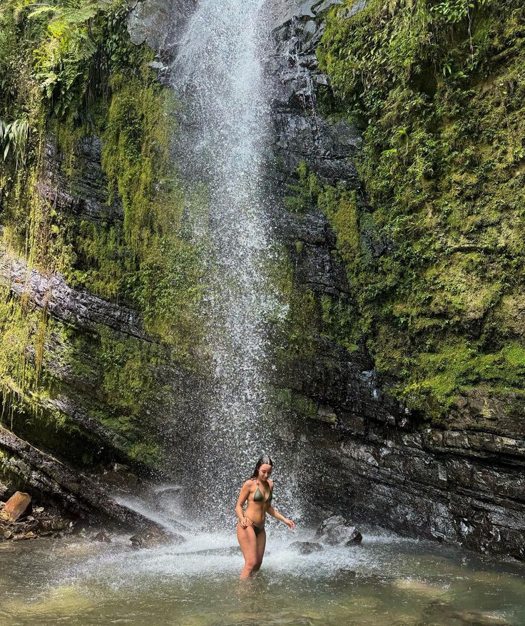 a woman standing in the water near a waterfall