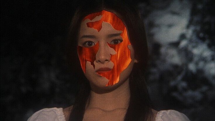 a woman with her face painted orange and white, standing in front of a dark background