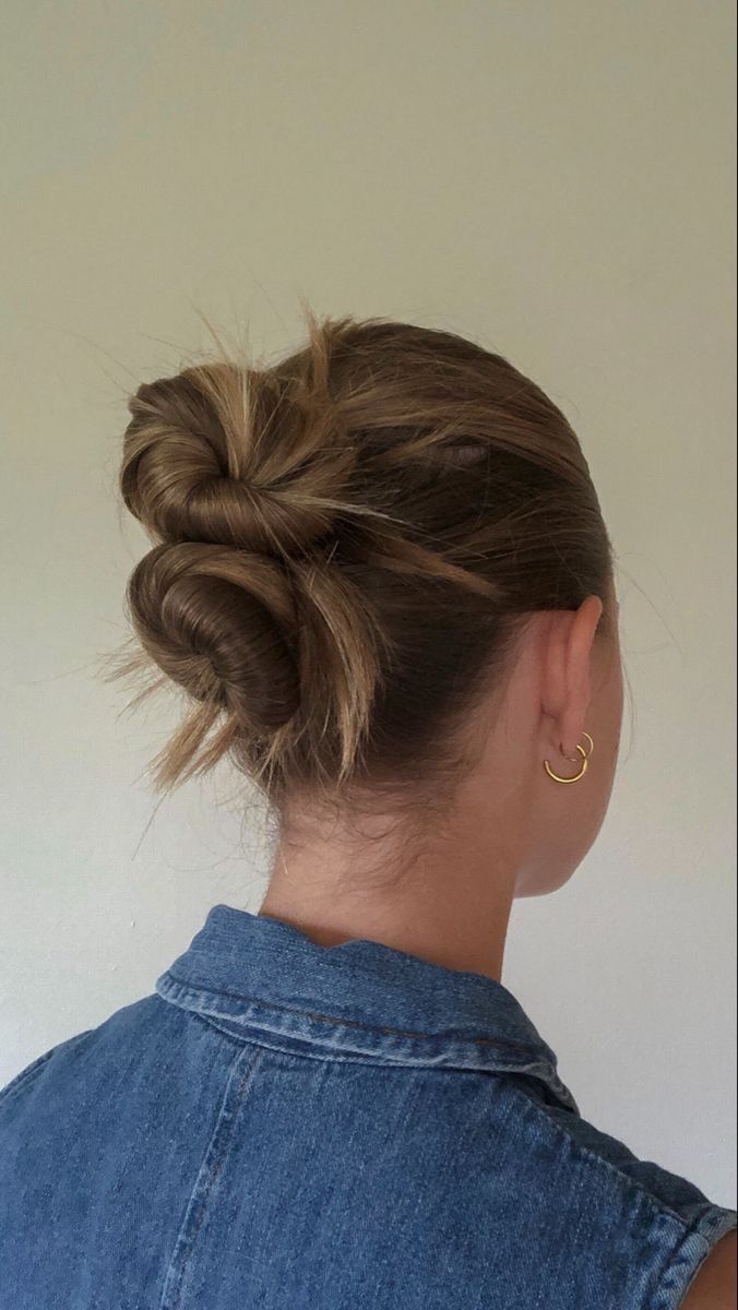 a woman with her hair in a low bun, wearing a denim shirt and gold hoop earrings