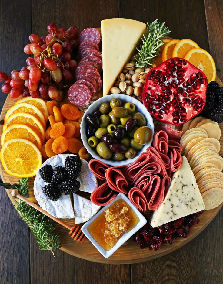 a platter filled with different types of cheeses, crackers and fruit on top of a wooden table