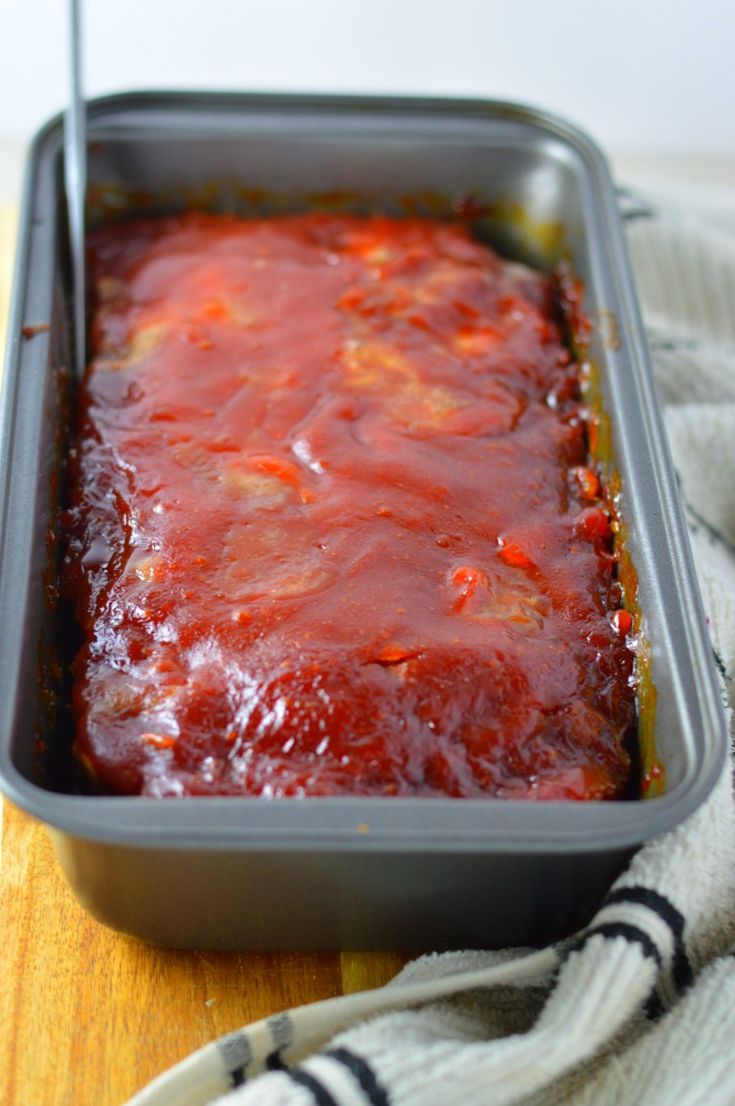 a casserole dish with sauce in it on top of a wooden table next to a striped towel