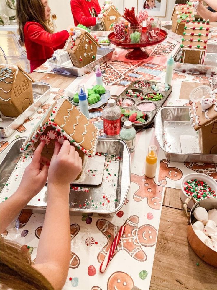 people making gingerbread houses at a table with christmas decorations and cookies on the table