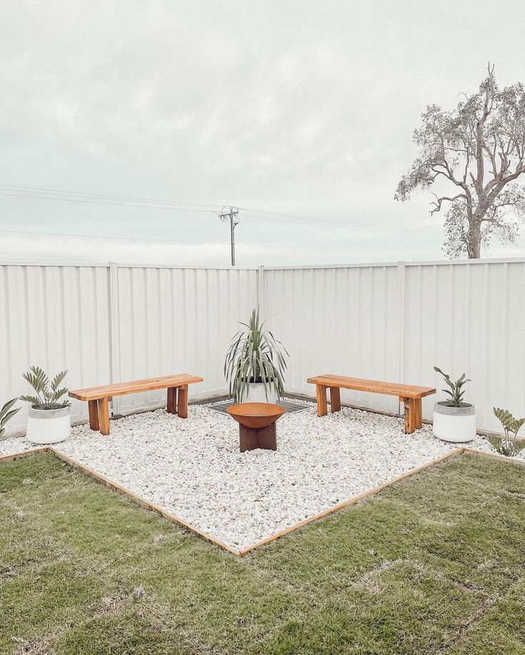 two wooden benches sitting next to each other on top of a patch of grass in front of a white fence