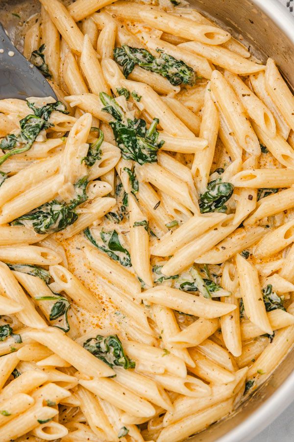 a pot filled with pasta and spinach on top of a table