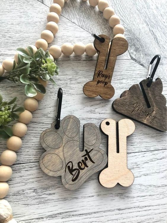 four wooden dog tags are shown on a white wood table with beads and plants in the background