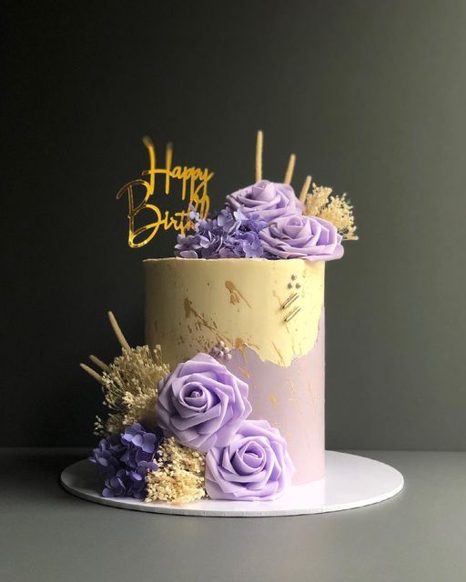 a birthday cake decorated with purple flowers and gold letters that say happy birthday on top