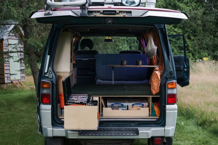 the back end of a van filled with luggage and boxes in grassy area next to trees