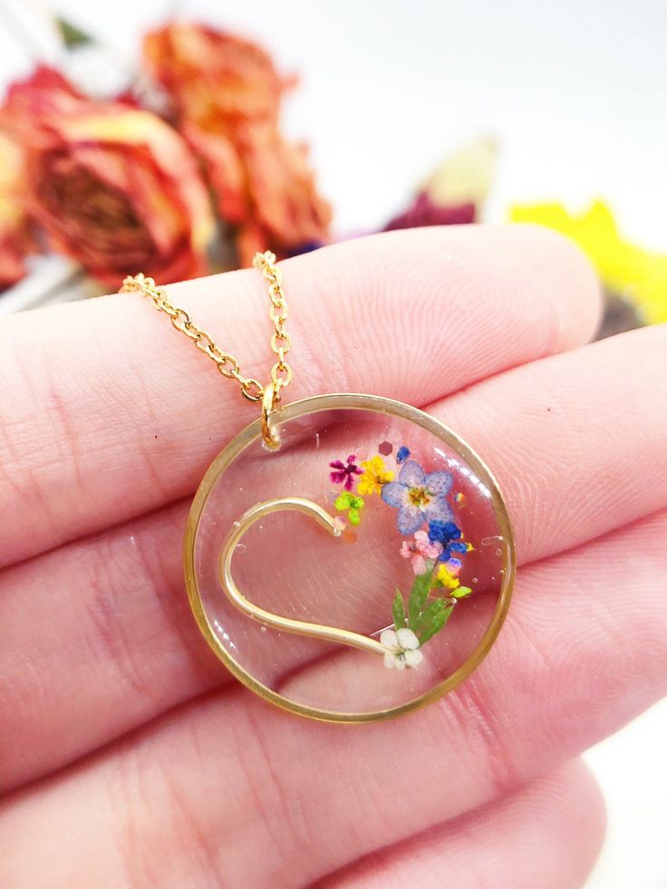 a hand holding a glass pendant with flowers in the shape of a heart on it