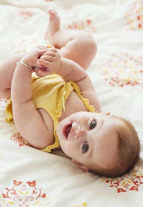 a baby laying on top of a bed wearing a yellow outfit and smiling at the camera