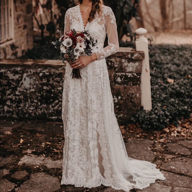 a woman standing in front of a stone building wearing a white dress and holding a bouquet