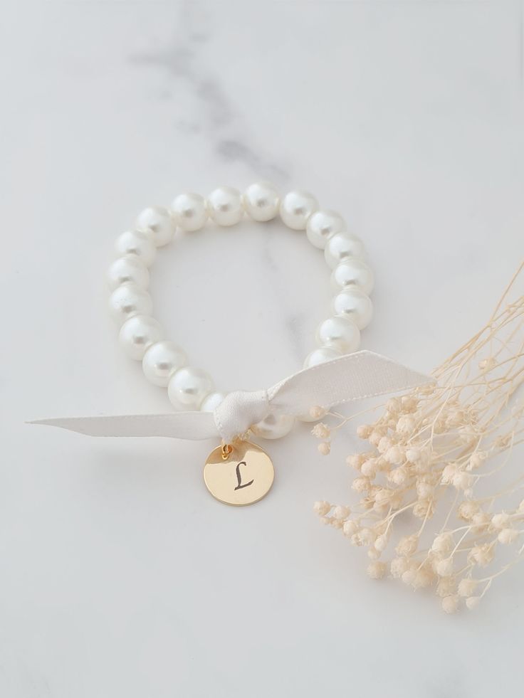 Personalised engraved initial pearl bracelet.  This bracelet features a gold stainless steel initial and ribbon tie in either cream or white. The pearls are available in cream or white and measure 8mm in diameter. This bracelet is stretchy and has no clasp so it can be slipped over the hand. Please see approximate size guide below: Sizes for children 12-24 months    5in 2-3 years    5.0-5.5in 4-5 years    5.75in 6-8 years    6in 9-13 years    6.25in Adult Sizes Small                  6.5in Mediu Adjustable White Monogram Jewelry, Elegant Adjustable Initials Charm Bracelet, Elegant Beaded Bracelets With Letter Beads For Gift, Elegant Beaded Bracelets With Letter Beads As Gift, Adjustable Ribbon Wedding Jewelry, White Monogram Jewelry For Wedding, White Monogrammed Jewelry For Wedding, White Monogram Wedding Jewelry, Elegant Charm Bracelet With Initials For Anniversary