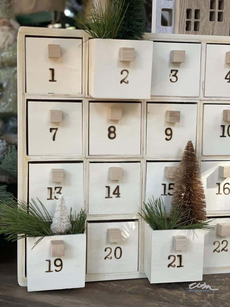 several white boxes with numbers and plants in them sitting on a wooden table next to christmas decorations