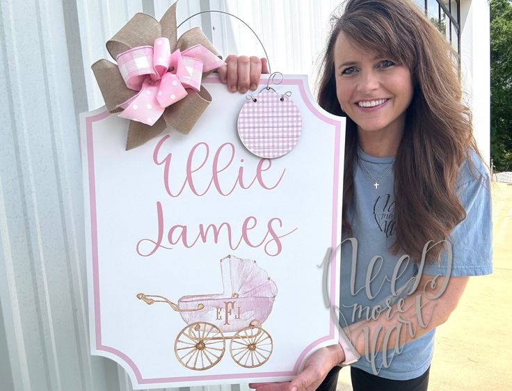 a woman holding up a sign that says welcome to her new baby with a pink carriage on it