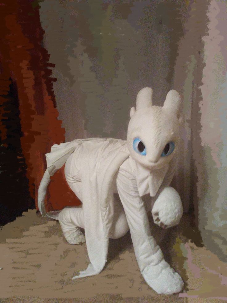 a white stuffed animal with big blue eyes on the floor in front of a wall