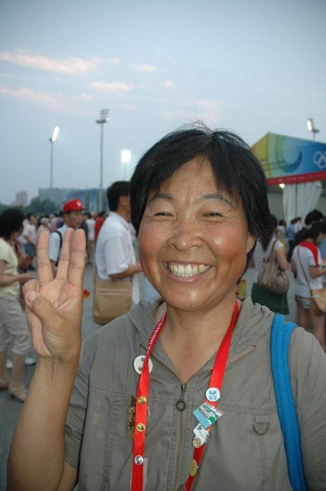 a woman is smiling and making the peace sign with her hand at an outdoor event