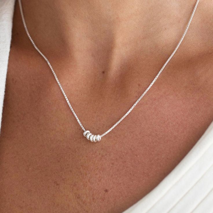 This is a stunning women's silver plated necklace will make a timeless addition to your collection. Featuring five tiny silver rings, this necklace makes a simple statement on its own, or can be layered with your other favorite silver neck wear. A classic and beautiful necklace that will suit any style of clothing, everyday or event.  Water resistance. Item will arrive in a pretty gift wrap, ready to give, with my brand logo. If you wish to view more silver necklaces - https://www.etsy.com/shop/jewelryforher2018?section_id=24105111 if you wish to view more items from this shop, visit: https://www.etsy.com/shop/jewelryforher2018 M3000022 / WN081 Silver Boho Necklace, Silver Necklace Simple, Necklace Bead, Layered Necklaces Silver, Silver Bead Necklace, Gold Bead Necklace, Bead Pendant, Beaded Pendant Necklace, Mothers Necklace