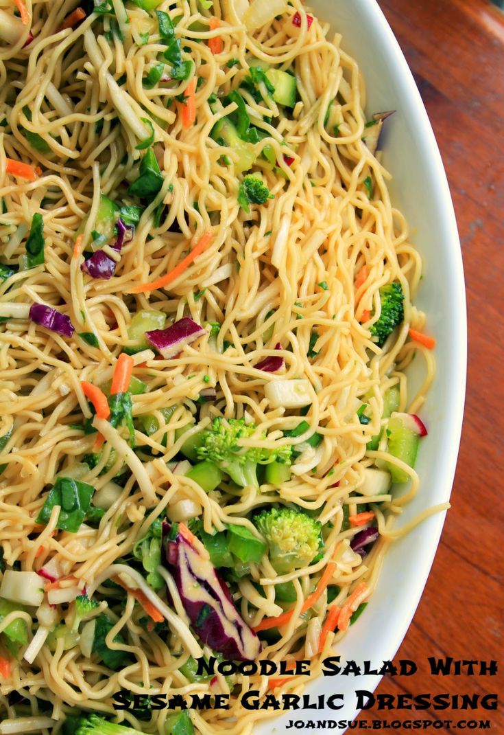 a white bowl filled with noodles, broccoli and carrots on top of a wooden table