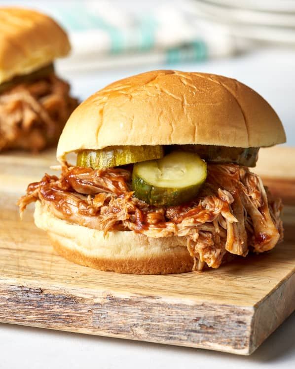 two pulled pork sandwiches with pickles on a cutting board