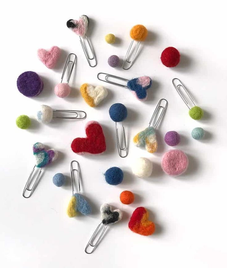 several different colored felt hearts and pins on a white surface