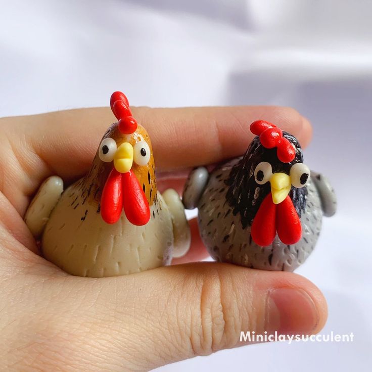 two small toy chickens sitting in the palm of someone's hand on a white background