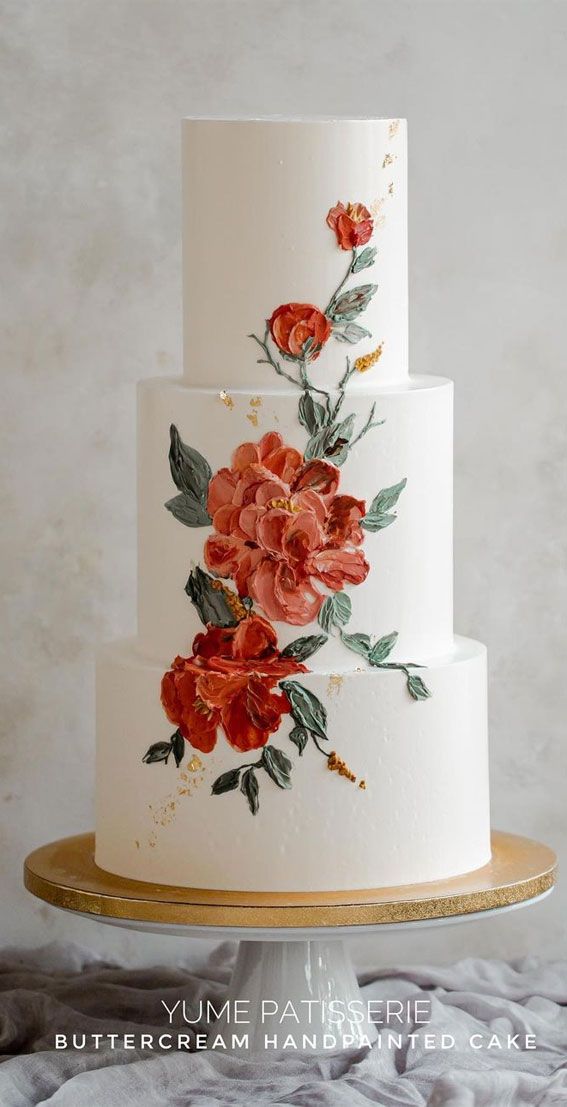 a three tiered white cake with red flowers on it and gold trimmings