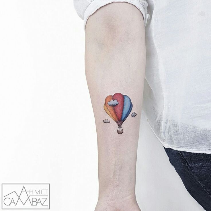 a person with a tattoo on their arm holding a hot air balloon in the shape of a heart